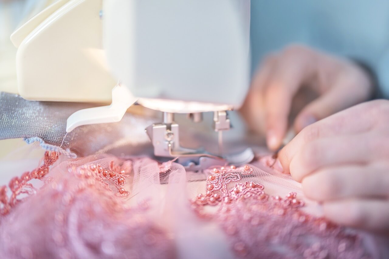 Close up of a man sewing a pink lacy piece of fabric on a sewing machine