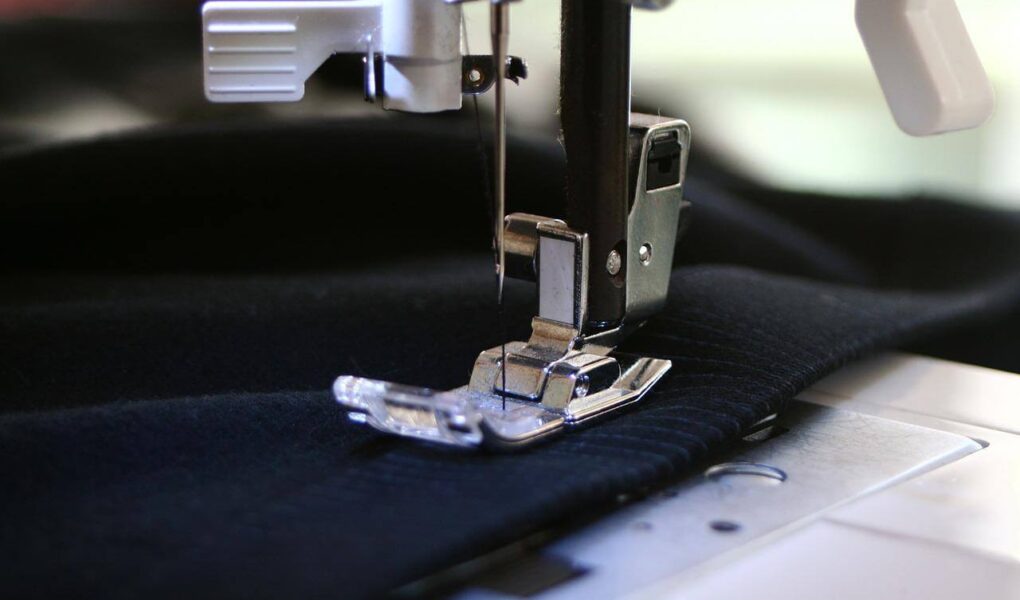 Close up of needle on sewing machine going over a dark blue garment that is laid across it
