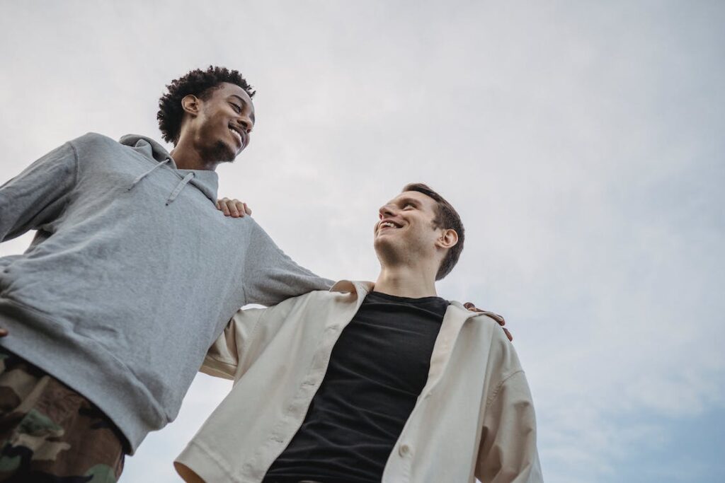 Free Happy young multiethnic male friends side hugging against cloudy sky Stock Photo